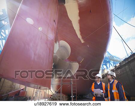 Stock Photo - Workers standing on shipbuilding site. Fotosearch