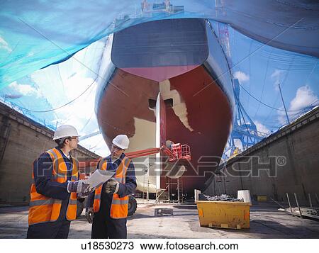 Stock Image - Workers talking at shipbuilding site. Fotosearch
