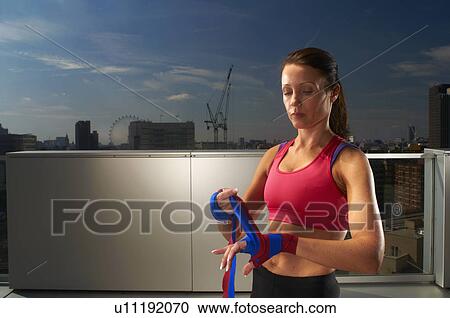 Stock Image - Boxer wrapping hands on urban rooftop. Fotosearch
