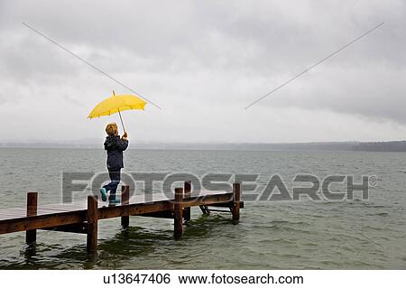 Boy carrying umbrella on wooden dock View Large Photo Image Stock Photograph - Boy carrying umbrella on wooden dock. Fotosearch