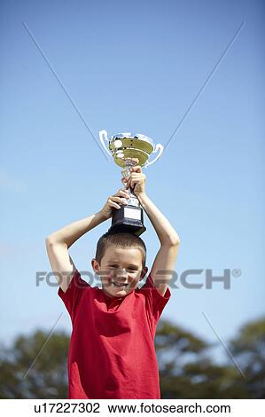 Stock Image - Boy cheering with trophy outdoors. Fotosearch