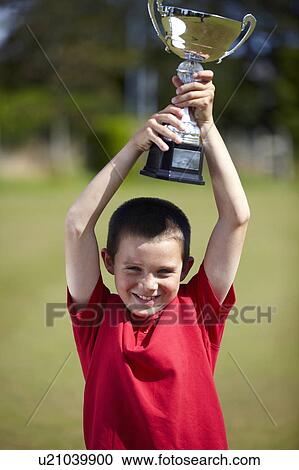 Stock Image - Boy cheering with trophy outdoors. Fotosearch