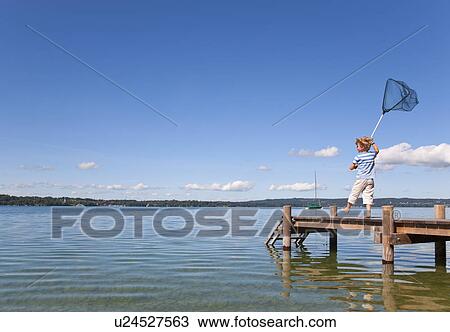 Stock Image - Boy fishing with net in lake. Fotosearch