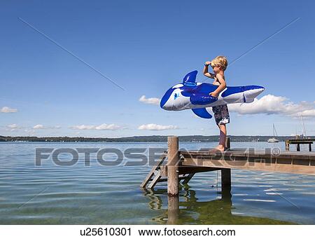 Stock Image - Boy holding inflatable whale on dock. Fotosearch