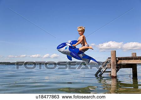 Boy jumping into lake with toy whale View Large Photo Image Stock Image - Boy jumping into lake with toy whale. Fotosearch