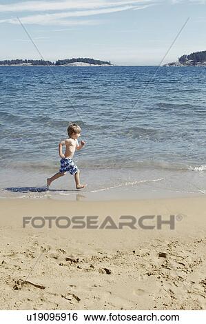 Stock Photograph - Boy running in waves on beach. Fotosearch