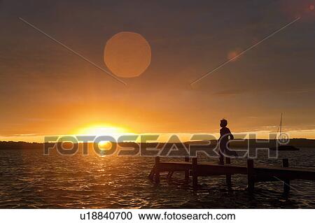 Stock Image - Boy running on wooden dock at sunset. Fotosearch