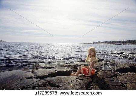 Stock Photo - Boy sitting on rocks by lake. Fotosearch