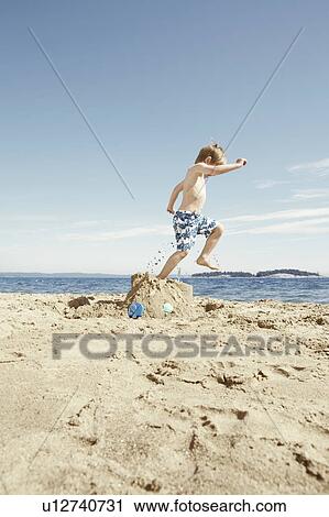 Stock Image - Boy stomping on sandcastle on beach. Fotosearch