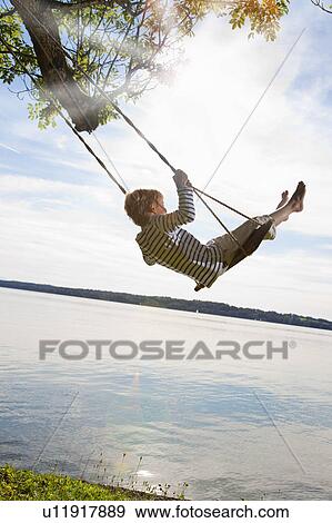 Boy swinging from tree by lake View Large Photo Image Stock Photo - Boy swinging from tree by lake. Fotosearch