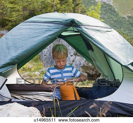 Stock Image - Boy unpacking sleeping bag in tent. Fotosearch