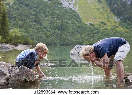 Picture - Boy washing his face in still lake. Fotosearch