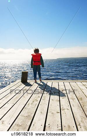 Boy wearing lifejacket on wooden pier View Large Photo Image Stock Photo - Boy wearing lifejacket on wooden pier. Fotosearch