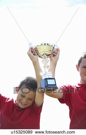 Stock Photo - Boys cheering with trophy outdoors. Fotosearch