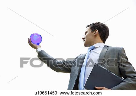 Stock Photo - Businessman examining globe outdoors. Fotosearch