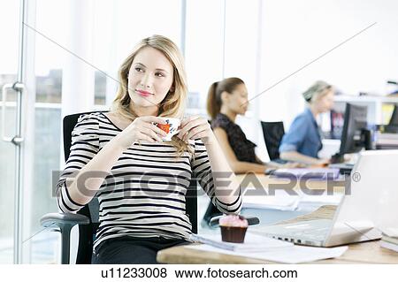 Stock Photo - Businesswoman drinking coffee at desk. Fotosearch