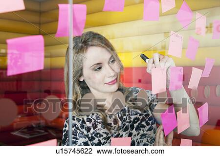 Stock Image - Businesswoman sticking notes on window. Fotosearch