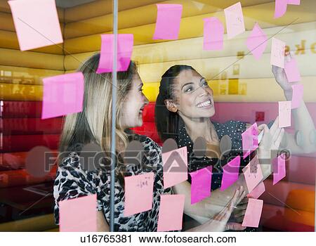 Businesswomen sticking notes on window View Large Photo Image Stock Image - Businesswomen sticking notes on window. Fotosearch