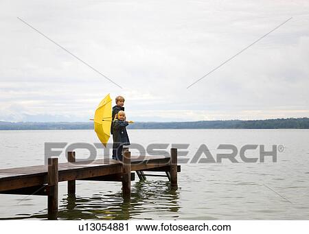 Stock Image - Children with yellow umbrella on dock. Fotosearch