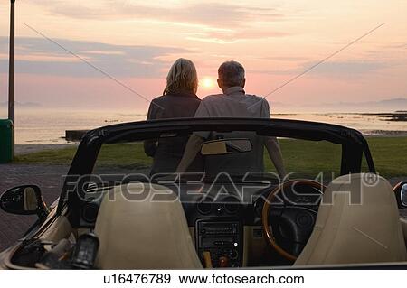 Stock Photo - Couple admiring sunset in convertible. Fotosearch