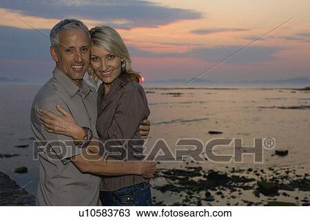 Stock Image - Couple hugging at sunset. Fotosearch