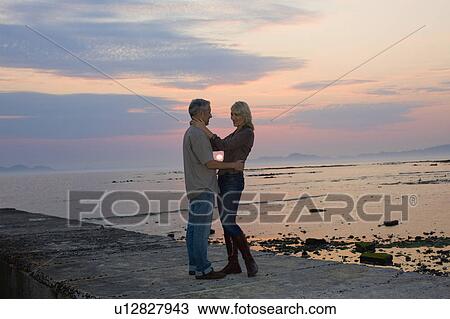 Couple hugging on pier at sunset View Large Photo Image Stock Image - Couple hugging on pier at sunset. Fotosearch