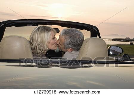 Couple kissing in convertible at sunset View Large Photo Image Stock Photo - Couple kissing in convertible at sunset. Fotosearch
