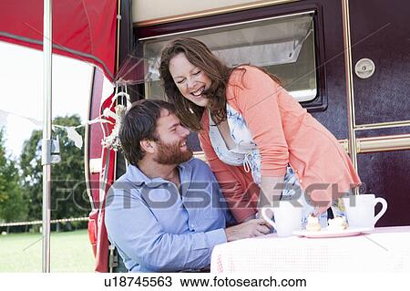Stock Image - Couple picnicking outside trailer. Fotosearch