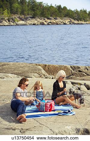 Picture - Family having picnic on rocks by lake. Fotosearch