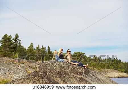 Stock Photo - Family sitting on rock by lake. Fotosearch
