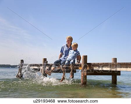 Stock Photo - Father and son dangling feet in lake. Fotosearch