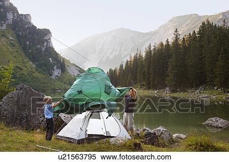 Stock Photography - Father and son pitching a tent by lake. Fotosearch