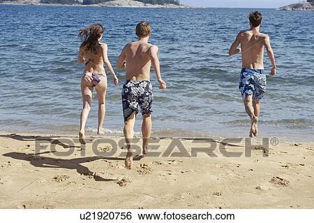 Stock Photograph - Friends running into ocean on beach. Fotosearch