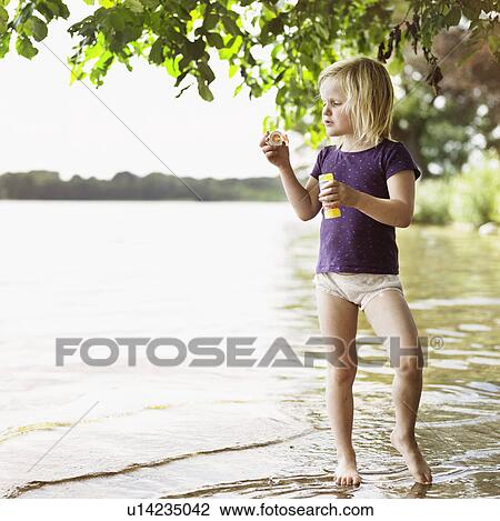 Stock Image - Girl blowing bubbles by lake. Fotosearch