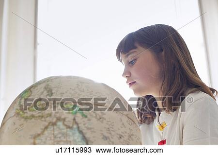 Stock Image - Girl examining globe indoors. Fotosearch