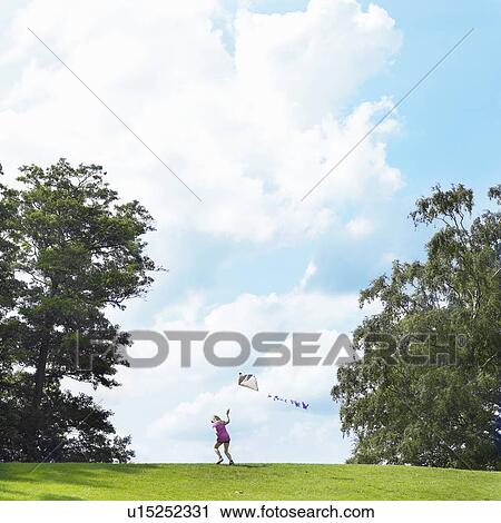 Stock Image - Girl flying kite in field. Fotosearch