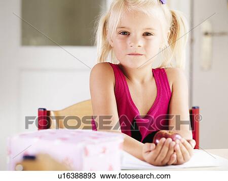 Girl holding an apple at desk View Large Photo Image Stock Image - Girl holding an apple at desk. Fotosearch