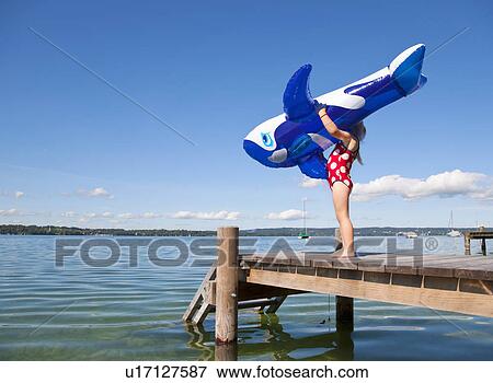 Stock Photo - Girl holding inflatable whale on dock. Fotosearch