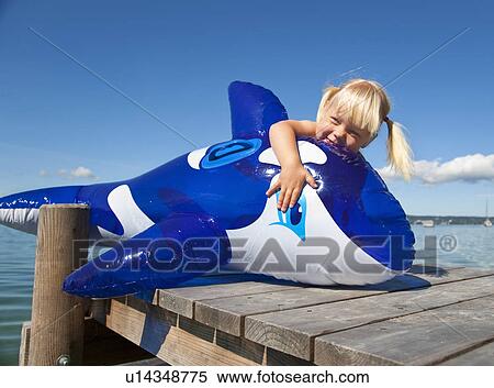 Stock Photography - Girl holding inflatable whale on dock. Fotosearch