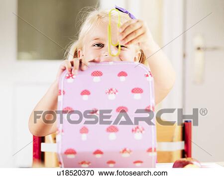 Stock Image - Girl holding oversize paper clip at desk. Fotosearch