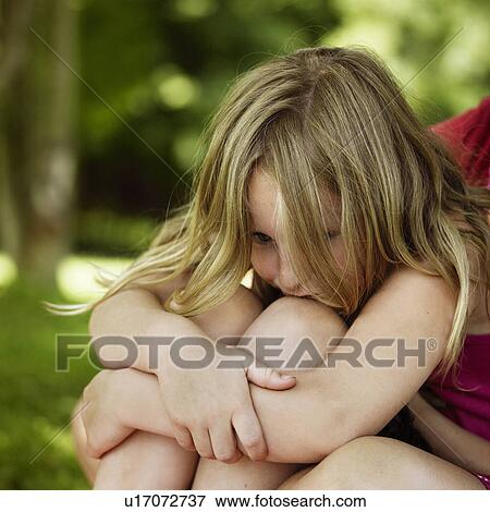 Stock Photo - Girl hugging her knees outdoors. Fotosearch