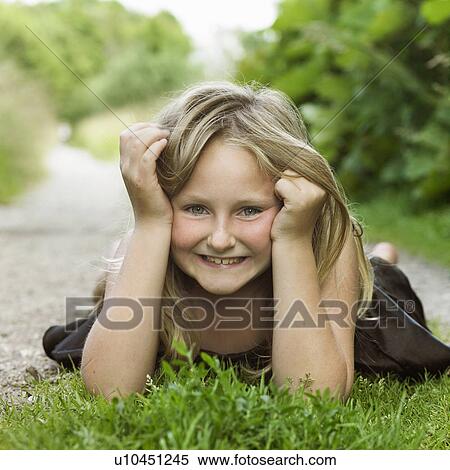 Stock Photography - Girl laying on grass in dirt path. Fotosearch