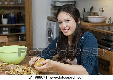 Stock Image - Girl peeling potatoes in kitchen. Fotosearch