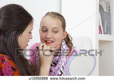 Stock Photo - Girl putting lipstick on friend. Fotosearch