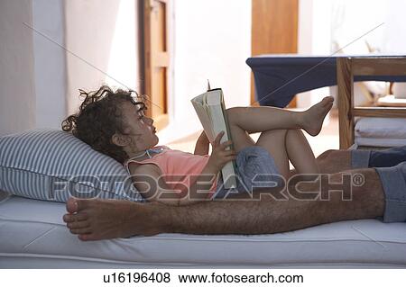 Girl reading with father on sofa View Large Photo Image Stock Photo - Girl reading with father on sofa. Fotosearch