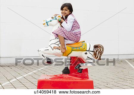 Stock Photo - Girl riding mechanical horse outdoors. Fotosearch