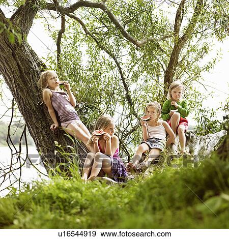 Stock Photo - Girls eating watermelon in tree by lake. Fotosearch