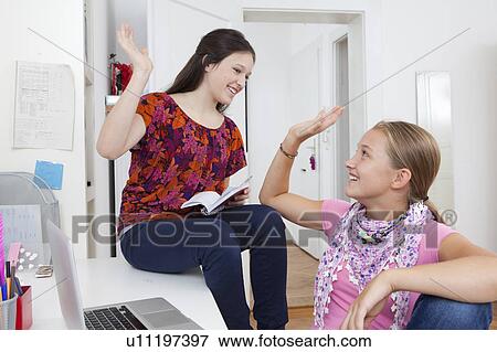 Stock Photo - Girls high fiving in bedroom at desk. Fotosearch
