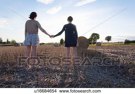 Picture - Girls holding hands in hay field. Fotosearch
