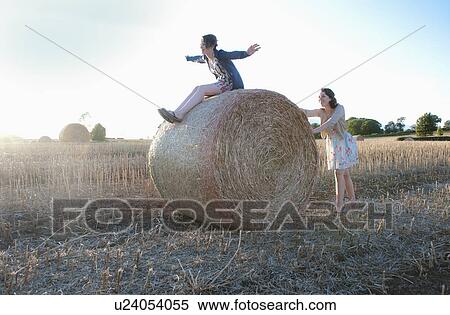 Stock Photography - Girls playing on hay bale in field. Fotosearch